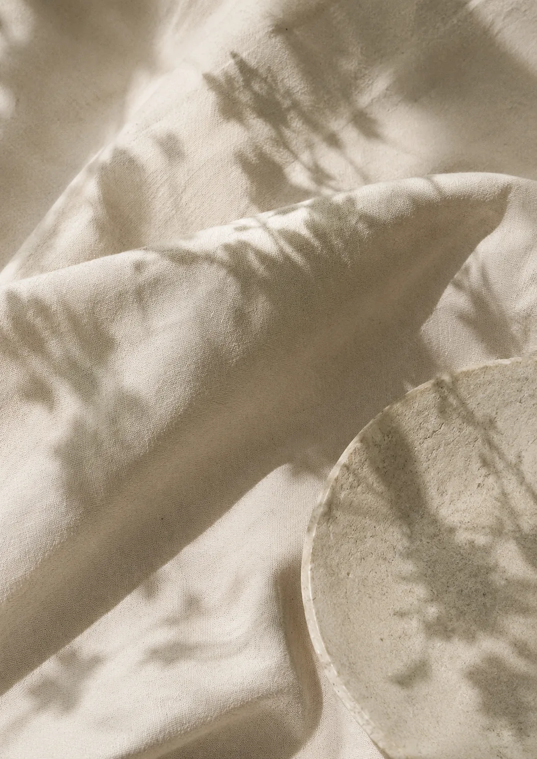 re:turn project visual: undyed cloth lying in soft folds, with the shadow of a plant falling across it.